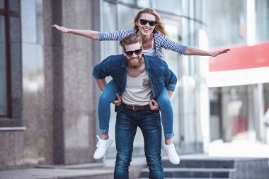 Kameraya bakarak ve açık havada duran süre gülümseyen güneş gözlüğü güzel genç çift. Kız Paketle