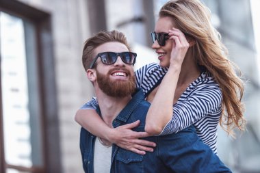 Birbirine bakarak ve açık havada duran süre gülümseyen güneş gözlüğü güzel genç çift. Kız Paketle