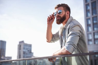 Güneş gözlüklü yakışıklı sakallı adam uzakta balkonda dururken arıyor