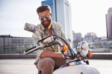 Güneş gözlüklü yakışıklı sakallı adam kameraya bakarak ve onun scooter üzerinde otururken gülümseyen