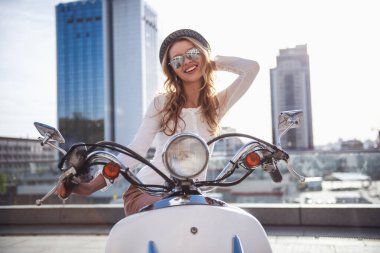 Güneş gözlüklü güzel kız kameraya bakarak ve bir scooter açık havada üzerinde otururken gülümseyen