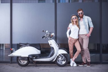 Güzel genç bir çift güneş gözlüğü, sarılma, kameraya bakıyor ve scooter açık havada yakın dururken gülümseyen