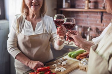 Güzel üst düzey iki önlük içinde şarap içmek, konuşmak ve birlikte mutfakta yemek yaparken gülümseyen