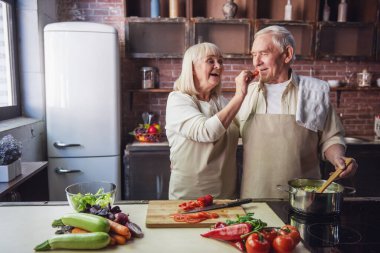 Güzel üst düzey iki önlük içinde yemek tatma ve birlikte mutfakta yemek yaparken gülümseyen