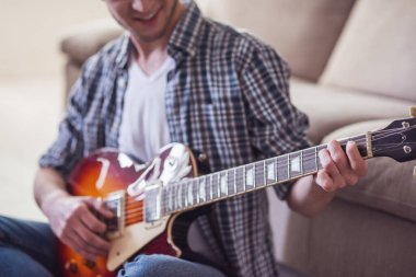 Gitar çalmak ve yerde evde otururken gülümseyen yakışıklı adam Resim kırpılmış