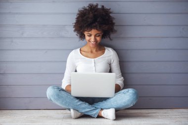 Çekici kız dizüstü bilgisayar kullanıyor ve yerde otururken gülümsüyor.