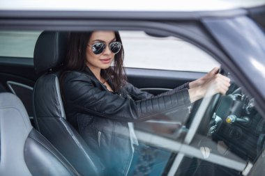 Deri ceket ve güneş gözlüklü güzel kız bir araba sürüş