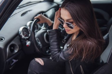 Deri ceket ve güneş gözlüklü arabasında oturan güzel kız