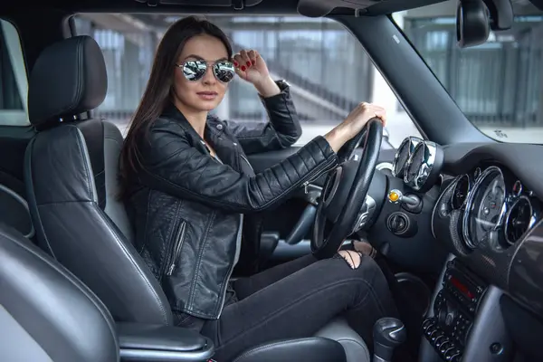 美丽的女孩在皮革夹克和太阳眼镜看相机在开车时 — 图库照片