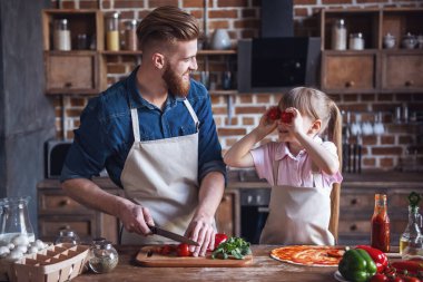 Sevimli küçük kız ve yakışıklı sakallı babası önlük içinde pizza mutfakta yemek yaparken gülüyorsun