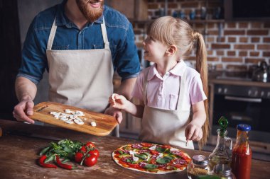 Sevimli küçük kız ve yakışıklı sakallı babası önlük içinde söz ve pizza mutfakta yemek yaparken gülümseyen
