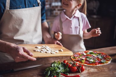 Sevimli küçük kız ve yakışıklı babası konuşmak ve pizza mutfakta yemek yaparken gülümseyen önlük içinde kırpılmış görüntü