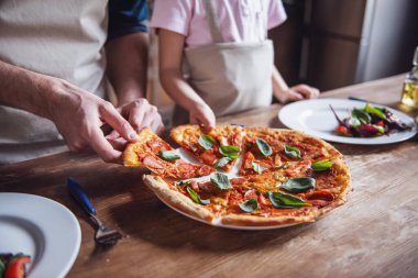 Küçük kız ve babası mutfağında sadece pişmiş pizza parçalarını alarak önlük içinde görüntü kırpılmış