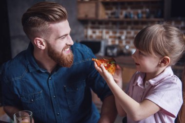 Sevimli küçük kız ve yakışıklı sakallı babası mutfakta pizza yerken gülüyorsun
