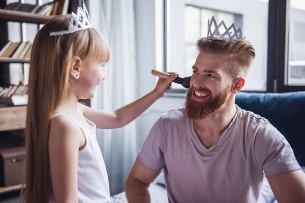 可爱的小女孩和她英俊的大胡子的父亲在冠微笑着在她的房间里玩 女孩做她的爸爸化妆 — 图库照片
