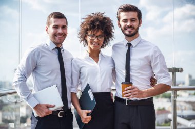 Güzel iş adamları kameraya bakıyor ve kahve molası sırasında bina ofis balkonda dururken gülümseyen