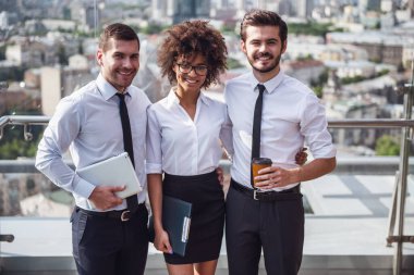 Güzel iş adamları kameraya bakıyor ve kahve molası sırasında bina ofis balkonda dururken gülümseyen