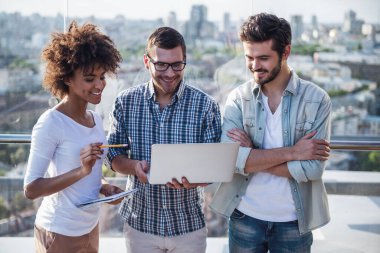 Güzel genç insanlar projeleri, dizüstü bilgisayar kullanarak ve şehir kurma balkonda çalışırken gülümseyen görüşüyorlar