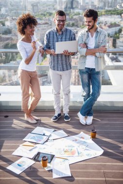 Güzel genç insanlar projeleri, dizüstü bilgisayar kullanarak ve şehir kurma balkonda çalışırken gülümseyen görüşüyorlar