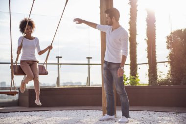 Güzel genç çift konuşuyor ve açık havada dinlenme süre gülümseyen, kız sallanıyor