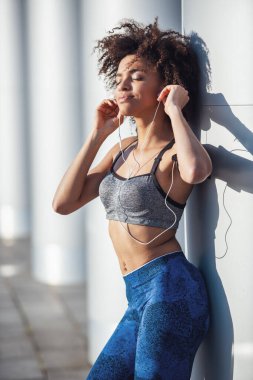 Spor kıyafetli ve kulaklıklı güzel kız sabah koşusunda dinlenirken gülümsüyor.