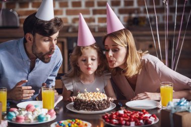 Mutlu anne ve kızı mumlar pastanın üzerine doğum günü kutlaması sırasında dekore edilmiş mutfak masasında otururken üfleme vardır