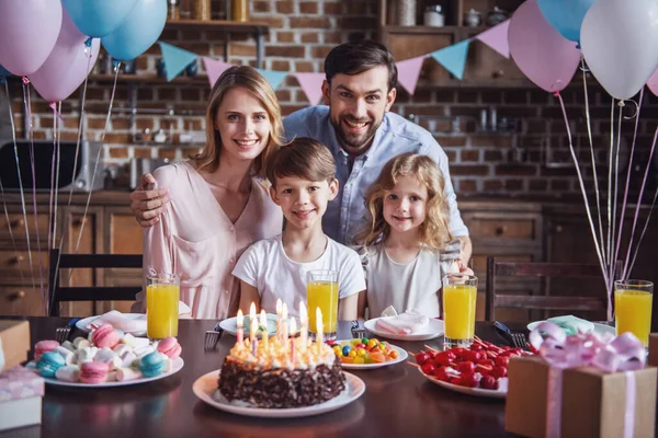 Portrait of happy family looking at camera and smiling while sitting at the table in decorated kitchen during birthday celebration