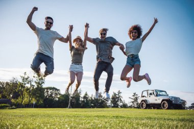 Mutlu genç insanlar, atlama ve güneşli havalarda açık havada dinlenme süre gülümseyerek elele