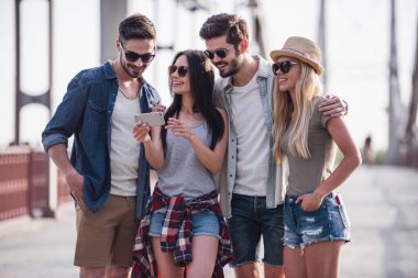 Neşeli genç insanlar konuşmak ve şehirde yürürken gülümseyen bir akıllı telefon kullanıyorsanız