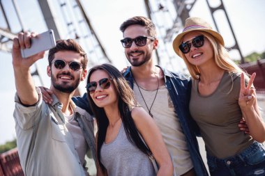 Neşeli genç insanlar bir akıllı telefon kullanarak ve açık havada yürürken gülen selfie yapıyorlar
