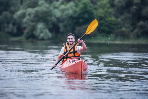 Handsome young man in sea vest is smiling while sailing a kayak
