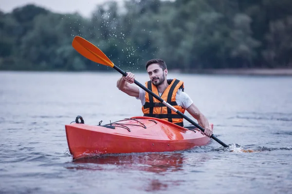 Handsome young man in sea vest is smiling while sailing a kayak