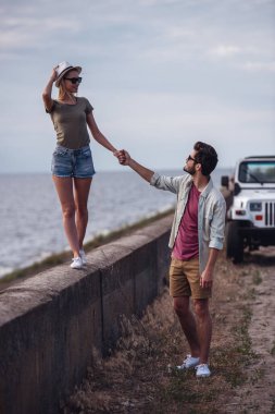 Güzel çift elele ve onların araba gezisi sırasında denize yakın yürürken gülümseyen