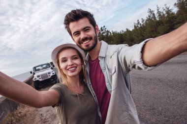 Güzel çift sarılma, kameraya bakıyor ve kendi araba gezisi sırasında denize yakın yürürken gülümseyen