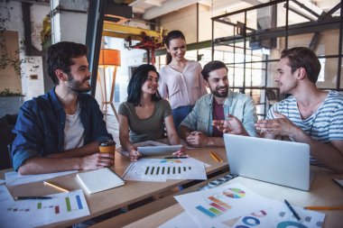 Güzel genç iş adamları rahat kıyafetler içinde konuşmak ve ofiste çalışırken gülümseyen bir dizüstü bilgisayar kullanıyorsanız