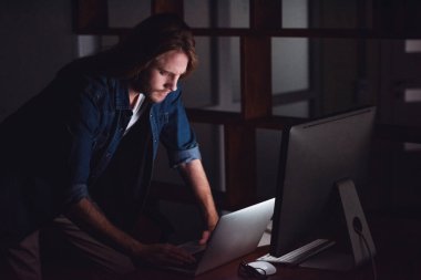 Yakışıklı genç işadamı ile omuz uzunlukta sarı saçları ve rahat kıyafet bir bilgisayarla geceleri çalışıyor