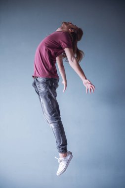 Omzuna ile şık genç adam sarı saçlı ve casual giyim atlama, gri arka plan üzerinde