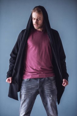 Omzuna ile şık genç adam sarı saçlı ve rahat kıyafetler içinde gri arka plan üzerinde şık kapşonlu hırka poz