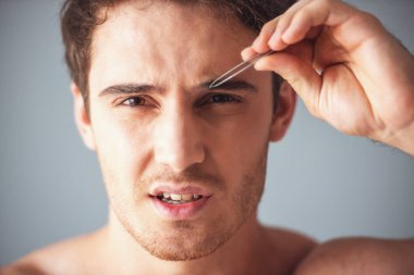 Çıplak omuz gri arka plan üzerinde kaşları koparma yapması ile yakışıklı genç adam portresi