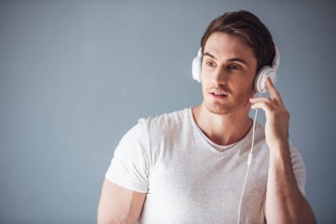 Yakışıklı genç adam rahat kıyafetler ve gri arka plan üzerinde kulaklık