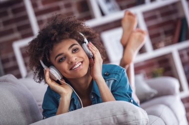 Kulaklıklı güzel kız evde kanepede yatarken müzik dinliyor ve gülümsüyor.