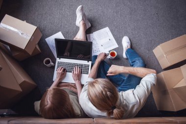 Güzel genç çiftin yukarıdan bir dizüstü bilgisayar kullanarak ve onların yeni daire iç karton kutular arasında katta otururken planlama