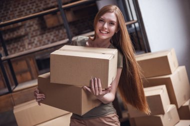 Güzel genç kadın karton kutular holding, kameraya bakıyor ve yeni daire içine hareket ederken gülümseyen