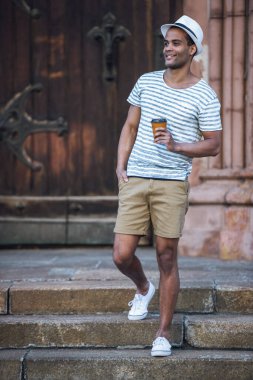 Şehirde yürürken elinde bir fincan kahve ve gülümseyen yakışıklı bir adamın tam boy portresi.