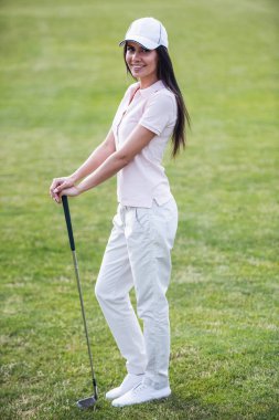 Tam uzunlukta bir golf kulübü holding, kameraya bakıyor ve golf sahası üzerinde dururken gülümseyen güzel genç kadın portresi