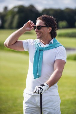 Yakışıklı bir golf kulübü holding, uzağa arıyorsunuz ve golf sahası üzerinde dururken gülümseyen