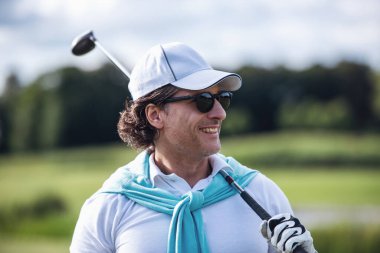 Yakışıklı bir golf kulübü holding, uzağa arıyorsunuz ve golf sahası üzerinde dururken gülümseyen