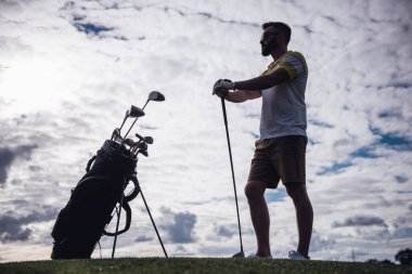 Tam uzunlukta bir golf kulübü tutarak ve uzak duran golf sahası üzerinde seyir yakışıklı adam portresi