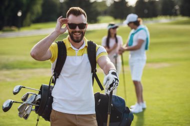 Güzel insanlar istirahat ve golf oynamak, yakışıklı adam ön planda kameraya bakıyor ve gülümsüyor