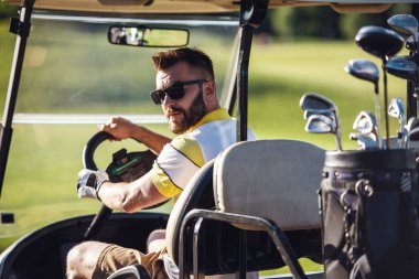 Yakışıklı olan bir golf arabası sürüş sırasında kameraya bakıyor